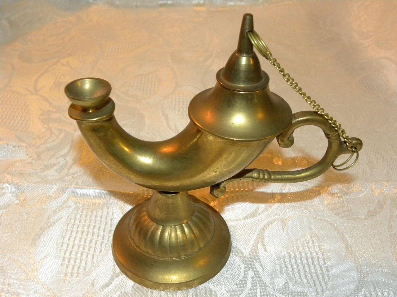 A white tablecloth with a brass oil lamp seated on top.