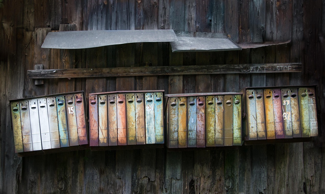 Rustic mailboxes attached to a wooden fence with tun roofing as a rain guard above them